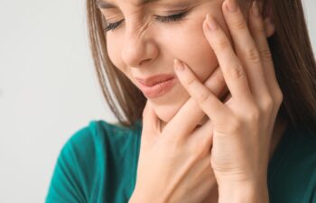 Young woman suffering from toothache against light background, closeup