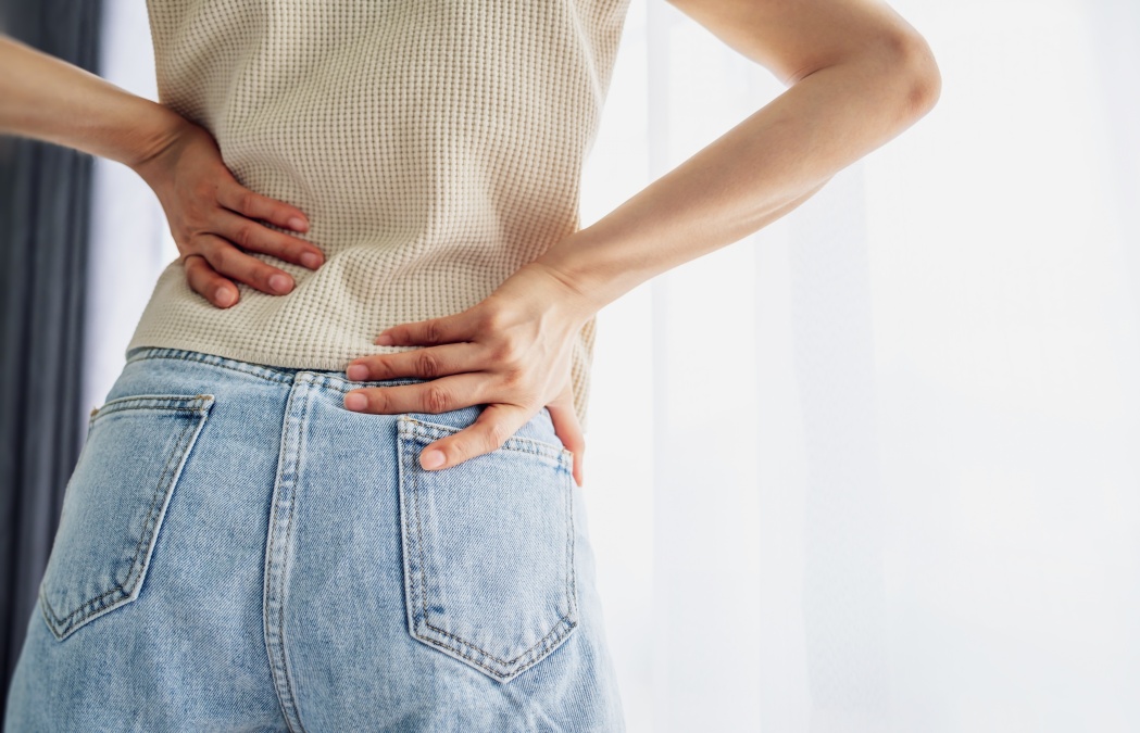 Woman standing holding her lower back suffering from chronic back pain. Healthcare and medical concept.