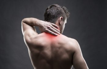 Pain in the neck. Man with backache. Muscular male body. Handsome bodybuilder posing on gray background with red dot