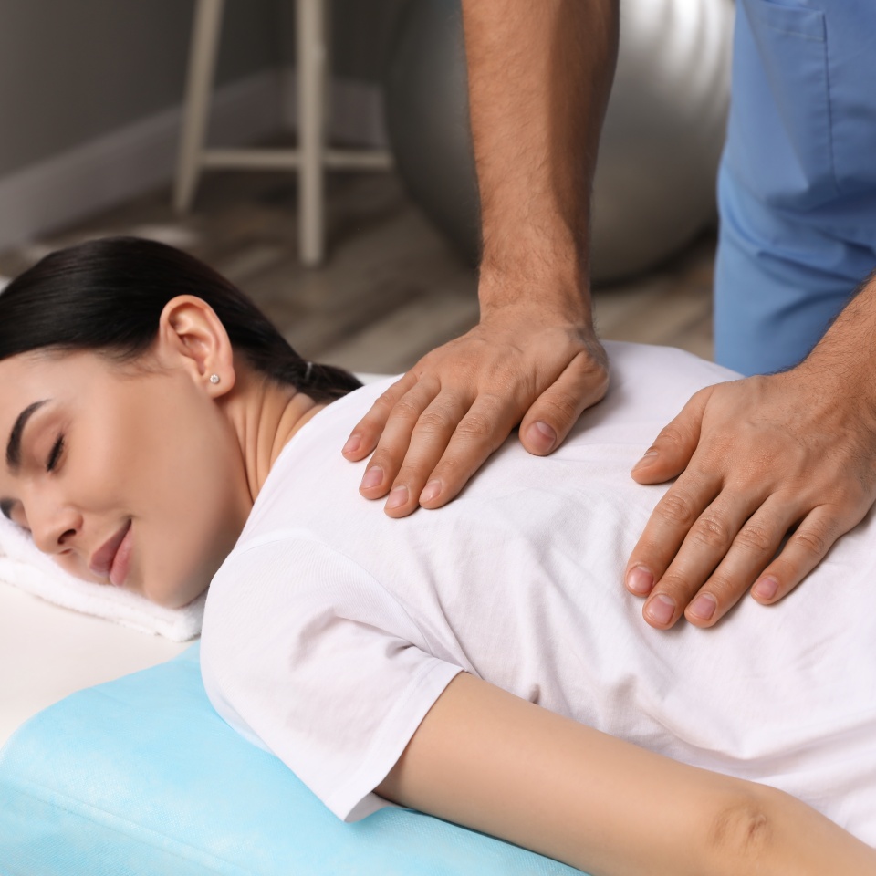 Orthopedist massaging young woman's back in clinic, closeup. Scoliosis treatment