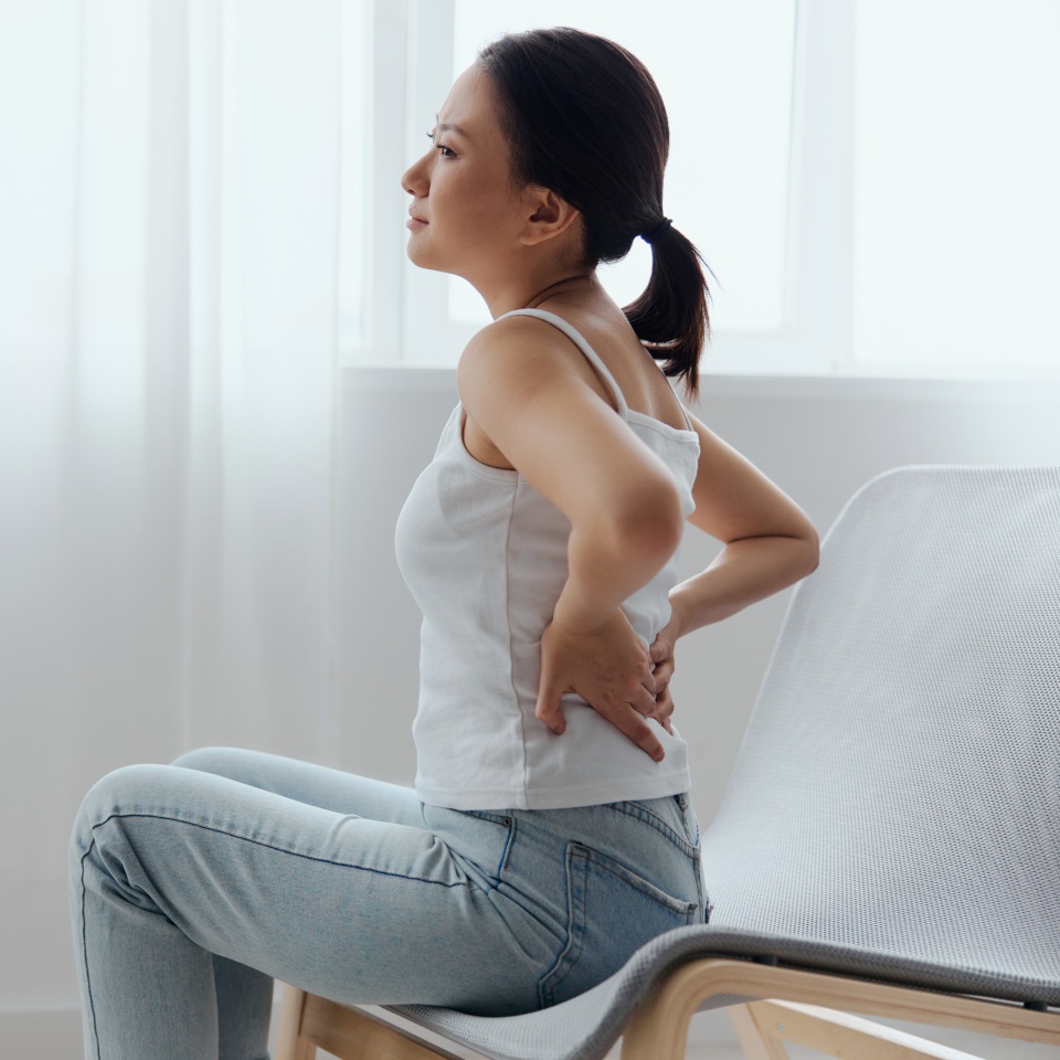 Suffering from scoliosis osteochondrosis after long study pretty young Asian woman feel hurt joint back pain laptop in incorrect posture sit on chair. Injuries Poor health Illness concept. Cool offer