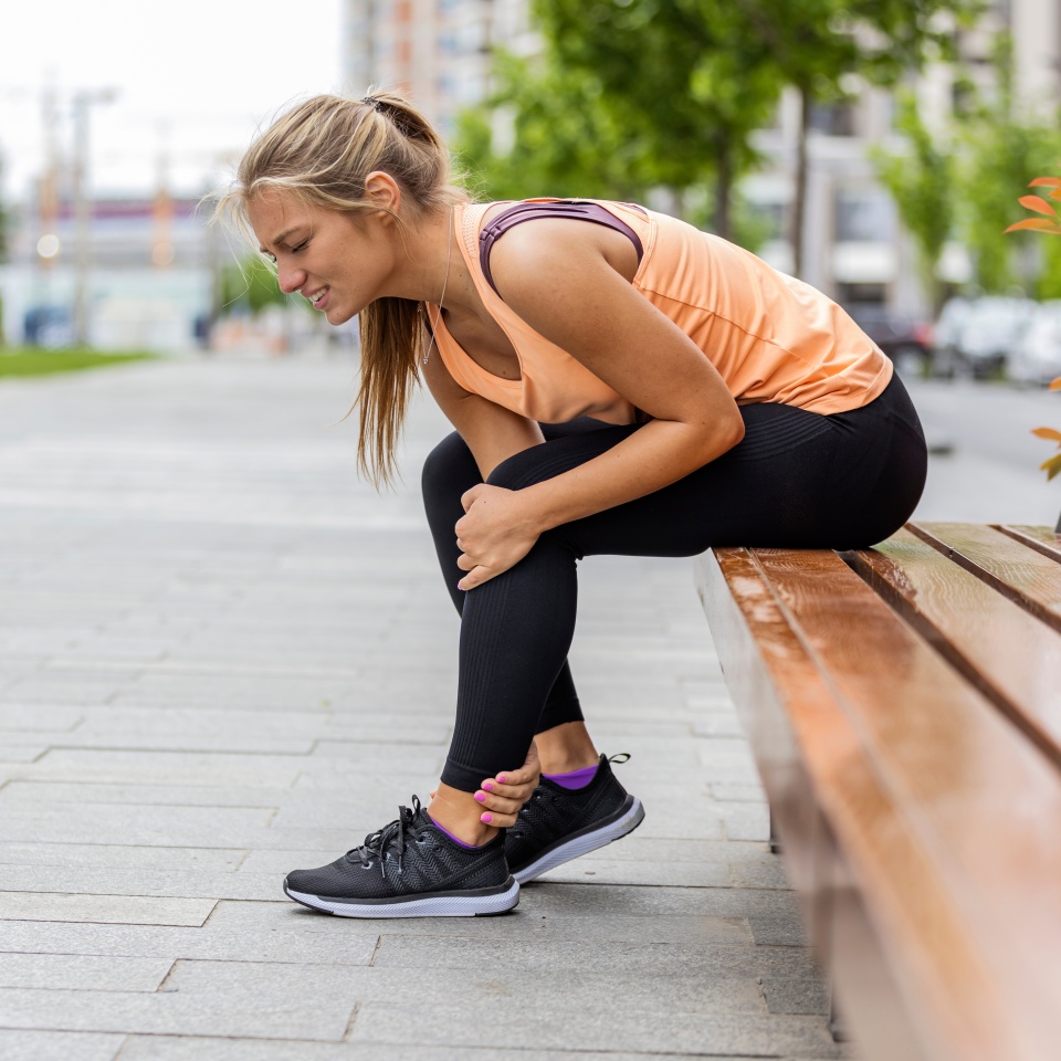 Running injury leg accident- sport woman runner hurting holding painful sprained ankle in pain. Athlete woman has ankle injury, sprained ankle during running training. Space for text