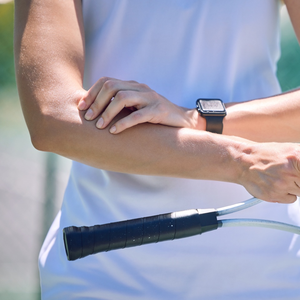 Sports, arm pain and tennis player with a racket and ball standing on a court during for a match. Closeup of a health, strong and professional athlete with equipment touching a medical elbow injury.