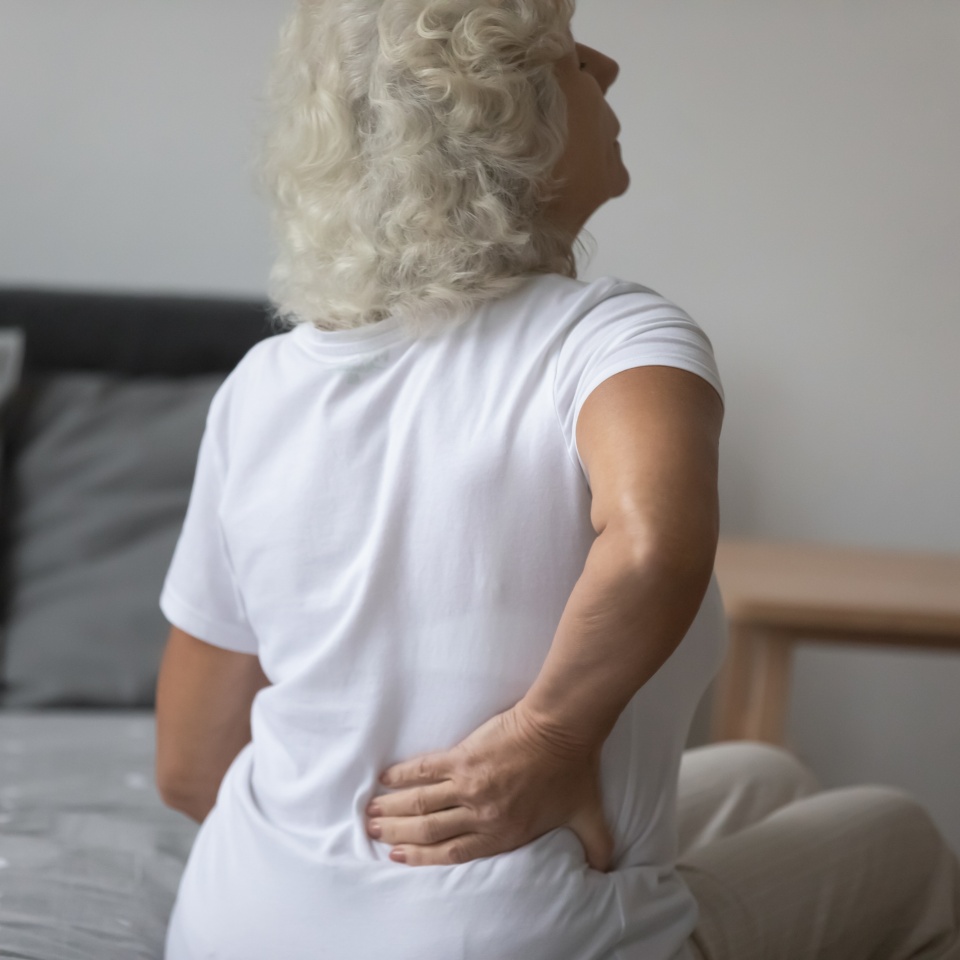 Rear view senior woman woke up touch lower back to reduce pain. Muscle spasm, tightness in pelvis, sharp ache kidneys infection, age related disease, osteoarthritis spinal stenosis treatment concept