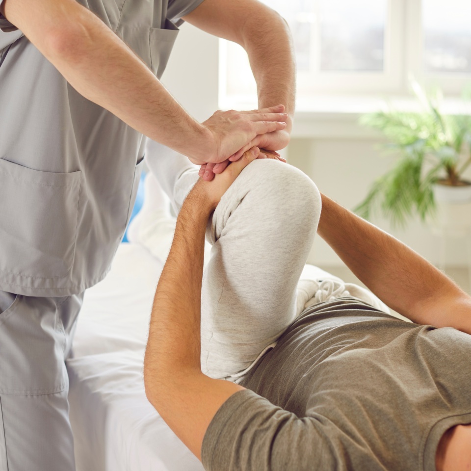 Male physical therapist doing healing treatment on mans knee in rehabilitation clinic. Professional physiotherapist or osteopath working in office. Physiotherapy and osteopathic medicine concept.