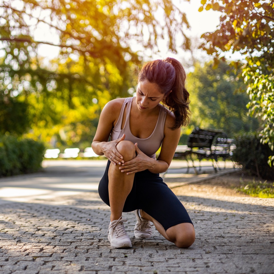 Young woman feeling pain in her knee. Woman runner got sports injury running on forest trail. Woman runner hold her sports injured knee.