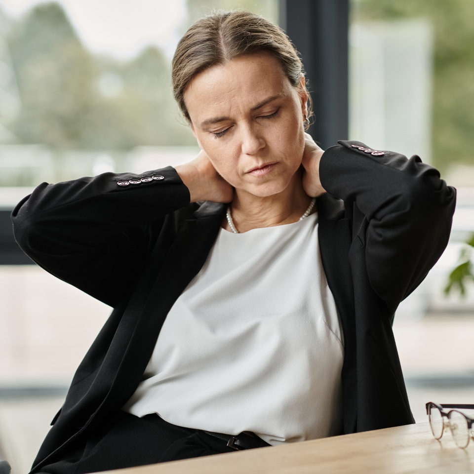Middle-aged woman with neck pain, stressed, sitting in front of laptop.