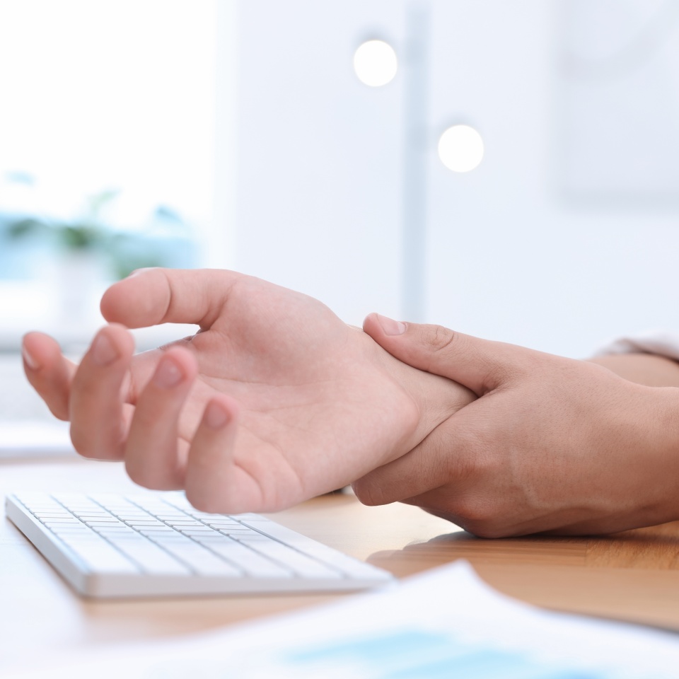 Man suffering from pain in wrist while working on computer at table indoors, closeup. Carpal tunnel syndrome