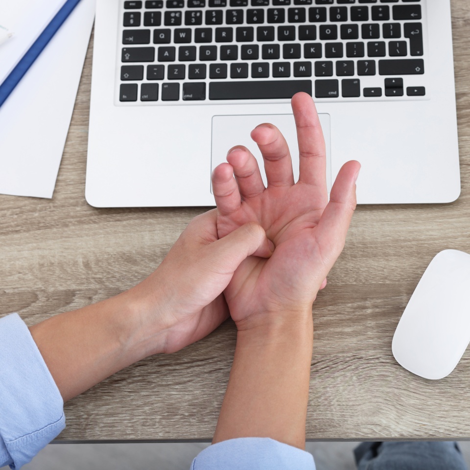 Man suffering from pain in wrist while working on laptop at wooden table, closeup, top view. Carpal tunnel syndrome