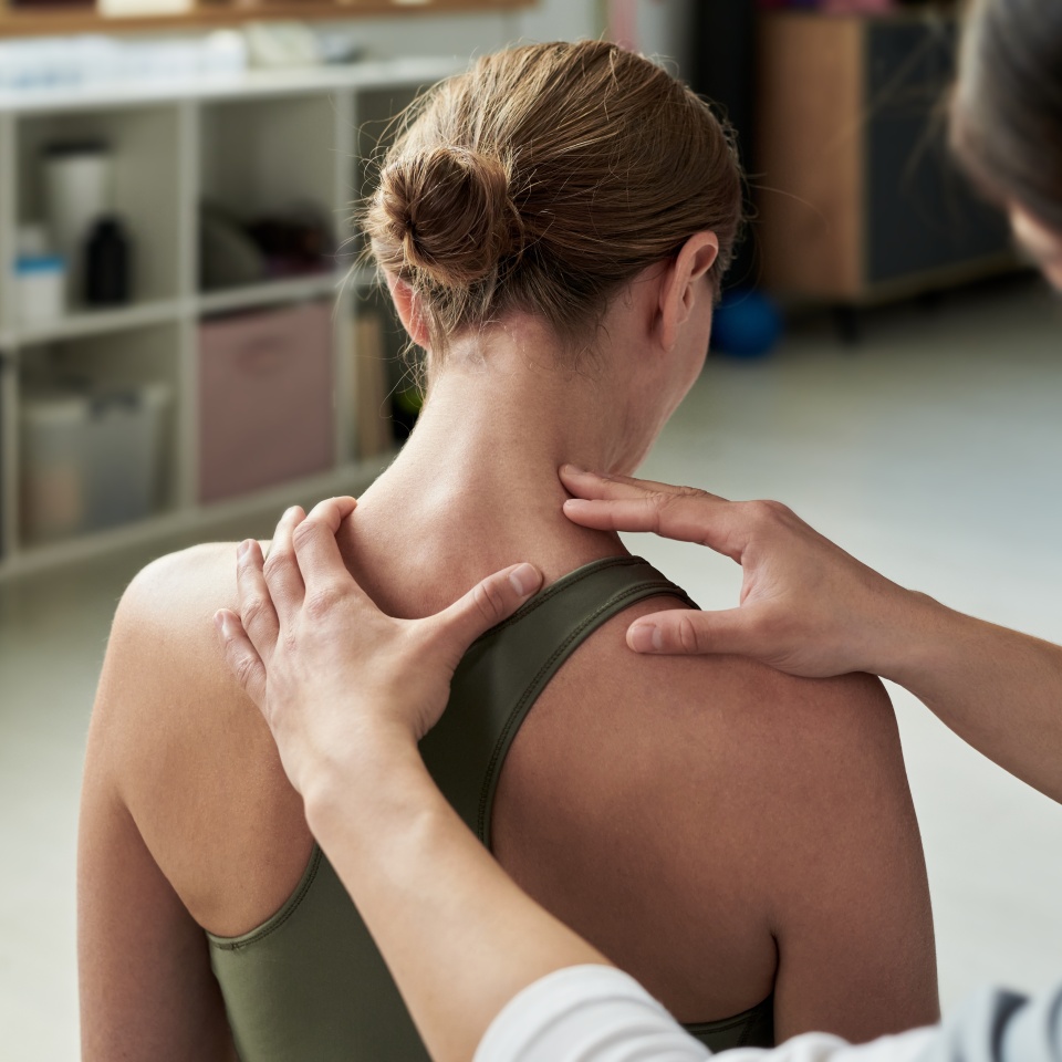 Physiotherapist giving patient spinal adjustment during therapy session in modern clinic. Patient undergoing treatment while seated on chair