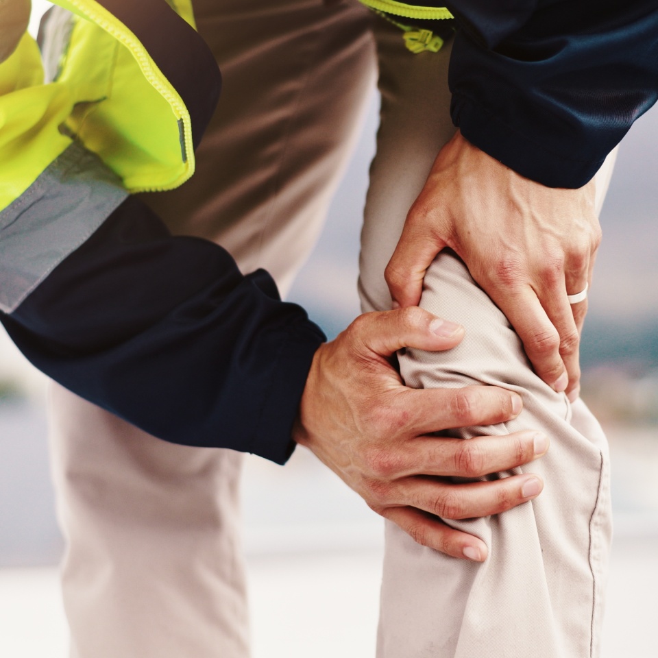 Person, architect and hands with knee pain for injury, construction accident or emergency in city. Closeup, civil engineer or contractor with joint inflammation, sore leg or sprain for arthritis