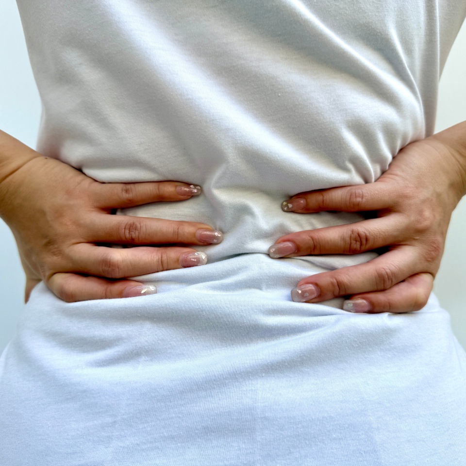 A woman pressing her back, possibly due to posture imbalance, muscle tension, or spinal issues. Symptoms might include pressure, mobility restrictions, or chronic pain