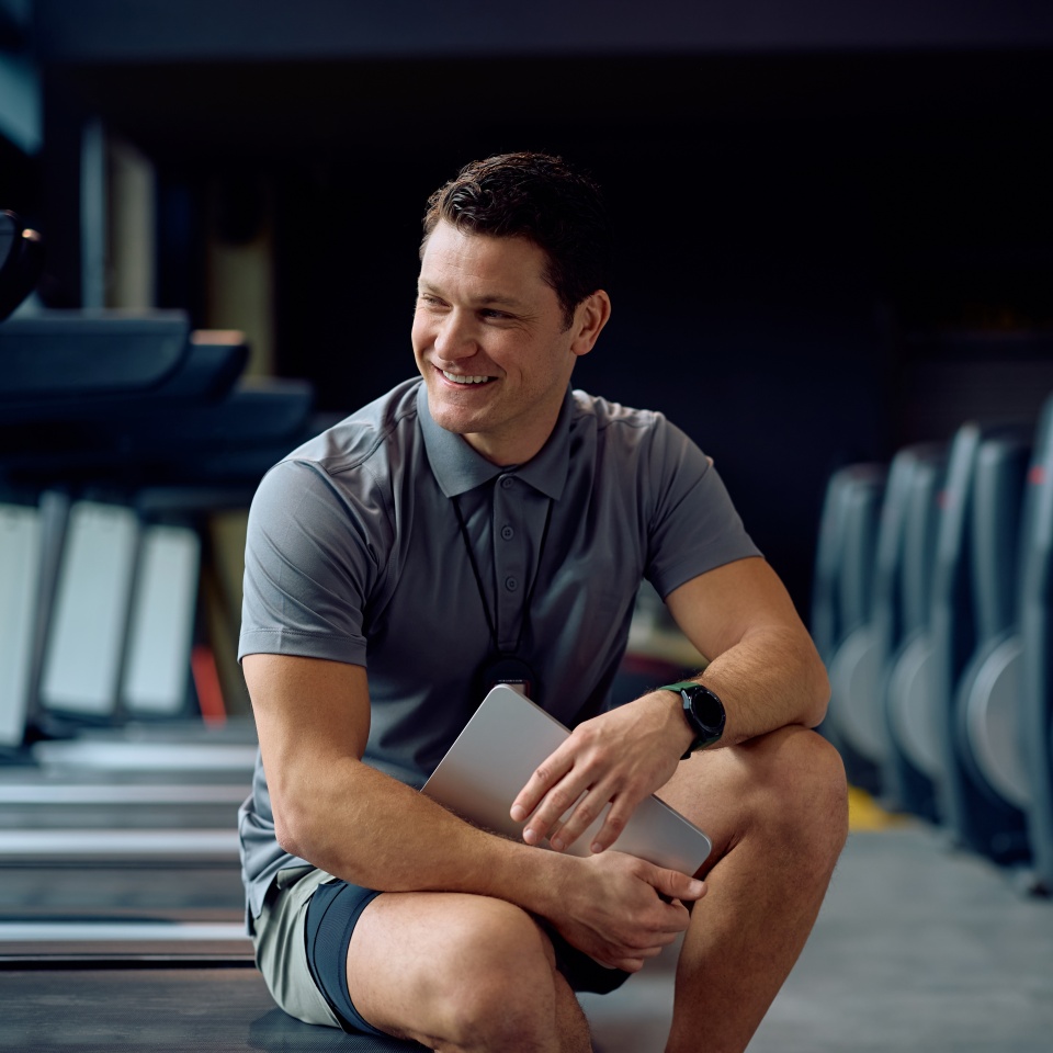 Happy fitness coach relaxing at health club and looking away. Copy space.