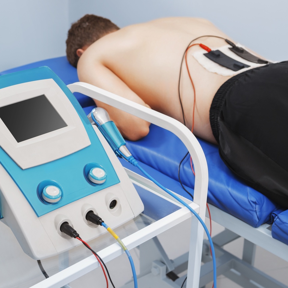 Electrotherapy treatment session with a patient lying on a medical bed. Electrical stimulation therapy using electrodes for pain relief and muscle rehabilitation in a physiotherapy clinic.