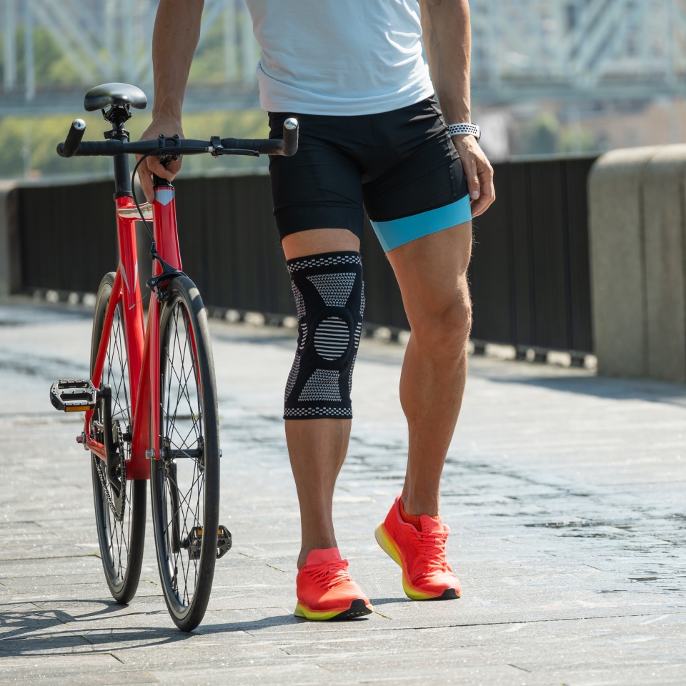 Cyclist walks with bandage on knee at public park. Unhappy cyclist with knee pain and injury outdoors.