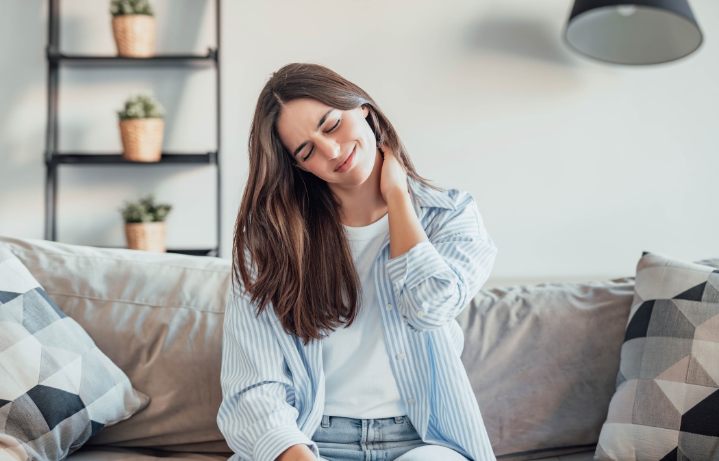 Unhappy young woman at home feeling painful neck ache, girl touching her neck muscles feeling fatigue and exhausted. Girl with discomfort on the sofa for bad posture