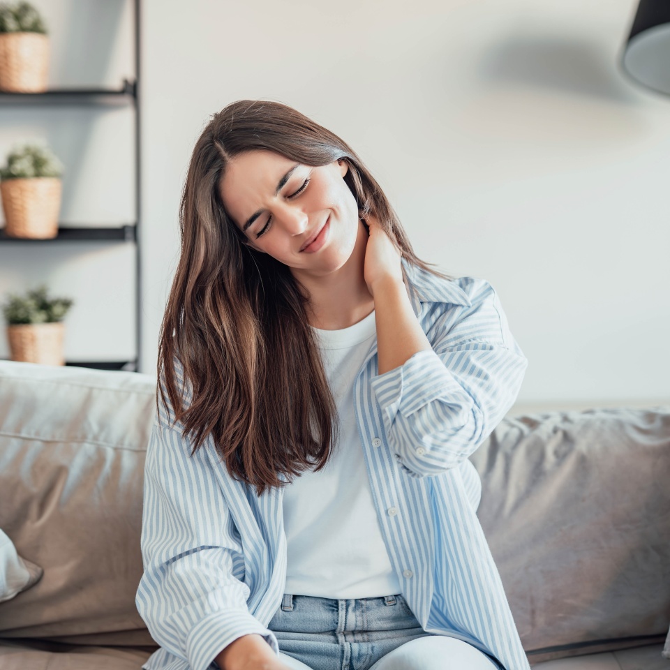 Unhappy young woman at home feeling painful neck ache, girl touching her neck muscles feeling fatigue and exhausted. Girl with discomfort on the sofa for bad posture