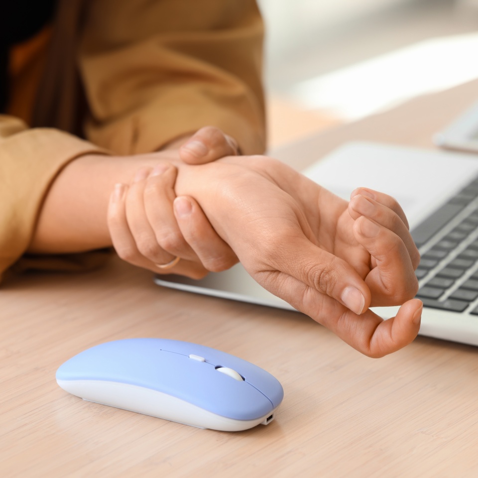 Woman suffering from pain in wrist at table in office