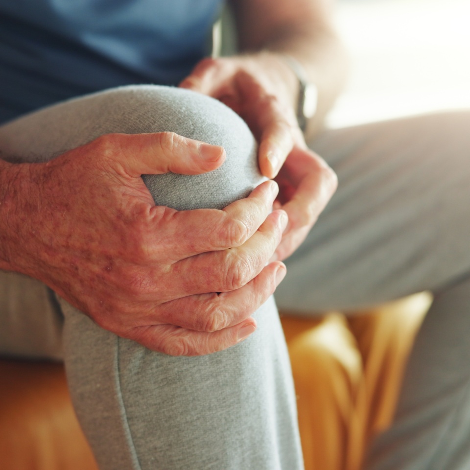 Knee pain, tension and hands of man in home for fibromyalgia, emergency and pressure crisis. Joint inflammation, osteoarthritis and sprain with person in living room of apartment for cramp and injury