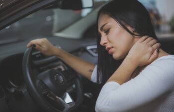 Beautiful young woman rubbing her neck, feeling sore after long drive. Female driver having terrible neck pain after whiplash injury in car crash. Healthcare, safety, pain concept
