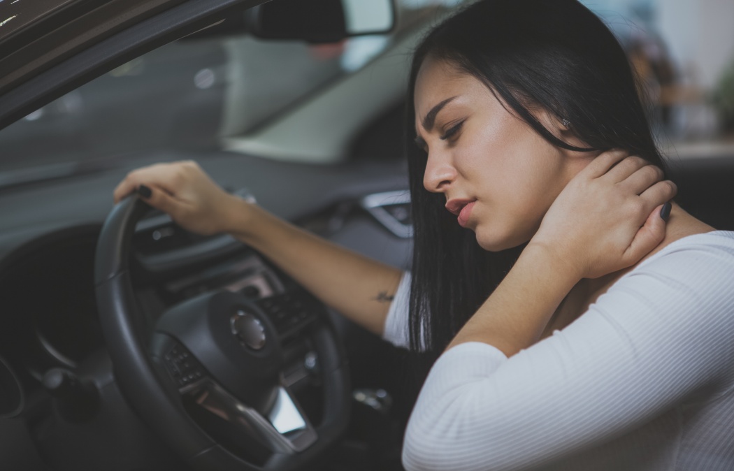 Beautiful young woman rubbing her neck, feeling sore after long drive. Female driver having terrible neck pain after whiplash injury in car crash. Healthcare, safety, pain concept