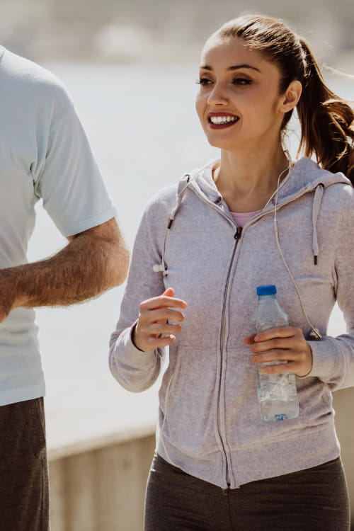 An older man and a younger woman jogging outdoors, each holding a water bottle.